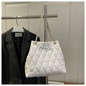 Close-up of white quilted tote bag with golden metal chain strap and leather texture