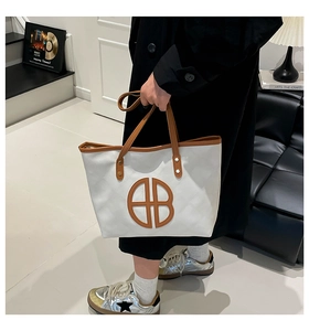 Detail of white quilted tote bag with brown trim and circular cutout logo design
