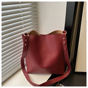 Close-up of matte dark red bucket bag featuring golden rivets and wide shoulder strap
