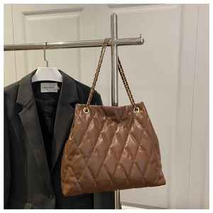 Detail of brown quilted leather tote bag with gold chain strap hanging on metal rack