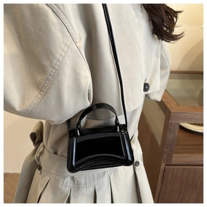 Détail du mini sac en cuir verni noir brillant avec base incurvée et fine bandoulière