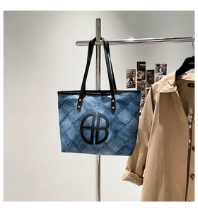 Detail of blue denim tote bag with quilted stitching and large leather logo patch