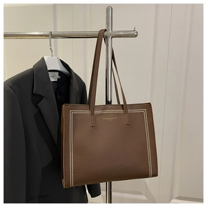 Detail of dark brown leather tote bag with white stitching and gold brand logo