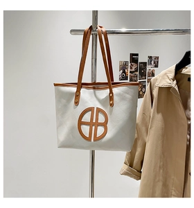 Detail of white tote bag with brown circular logo and slim handles on a hanger