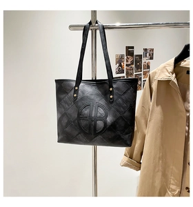 Detail of black quilted tote bag with circular logo hanging on a silver metal display stand