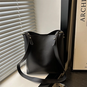 Minimalist black leather bucket bag with gold hardware detail and elegant shoulder strap