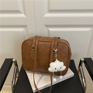 Retro brown leather bowling tote bag with a white plush charm on a black chair