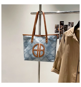 Detail of blue denim tote bag with brown leather handles and large AB circular logo