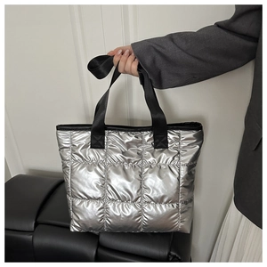 Detail der silbernen Puffer-Tasche mit Steppmuster und schwarzen Gurtbandgriffen