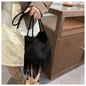 Détail d'un sac seau noir en daim avec de longues franges et une fine bandoulière élégante