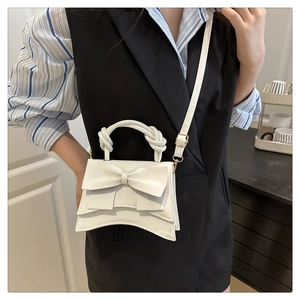 Close-up of a white bow shoulder bag with a woven handle shown on a model's side