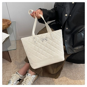 Detail of white quilted tote bag featuring silver bow accent and metallic studs