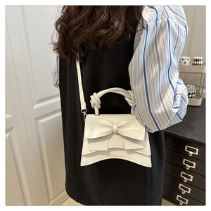 Detail of white PU leather crossbody bag with knot handle and decorative bow accent