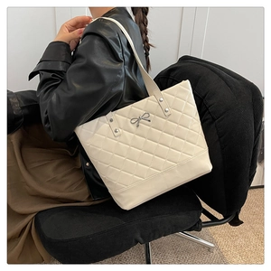 Detail of cream quilted tote bag with silver bow accent worn by model for daily commute