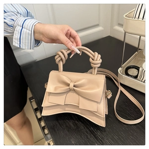 Detail of beige bow-knot handbag with elegant curved base and knot handle design