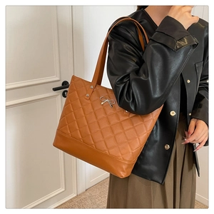 Brown quilted tote bag with silver bow accent worn over the shoulder by a model