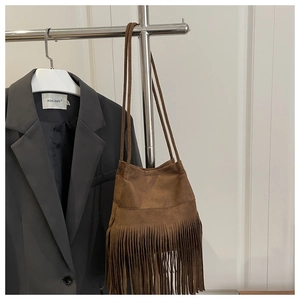 Sac bandoulière en daim marron avec longues franges devant une veste de costume sombre