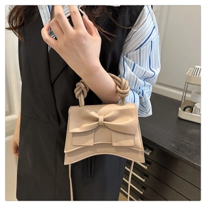 Detail showing the large bow design and twisted ring handle of the beige crossbody bag