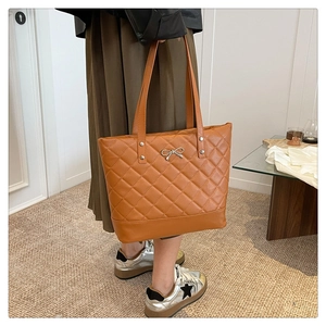 Close-up of quilted caramel tote bag with silver bow detail and long shoulder straps