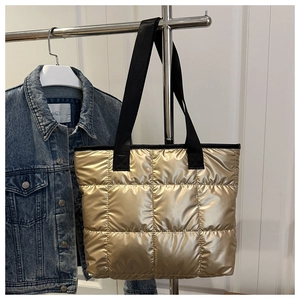 Detail einer gesteppten Puffer-Tasche in Metallic-Gold mit schwarzen Textilschultergurten