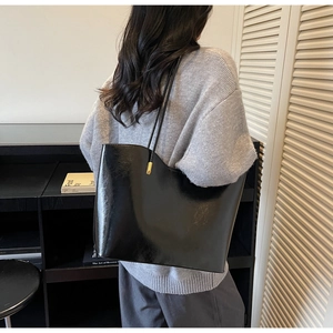 Side view of a large black glossy leather tote bag with wavy edges and gold hardware