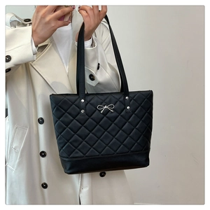Close-up of black quilted tote bag featuring silver bow charm and elegant diamond pattern