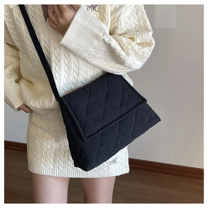 Detail of black quilted nylon crossbody bag with meticulous stitching on a white sweater