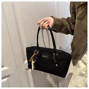 Detail of black faux suede tote bag featuring a gold fashion logo and wood bead tassel