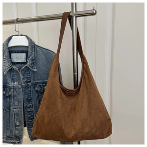 Detail of a large brown suede tote bag on a display rack with a denim jacket background