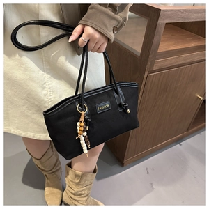 Detail of black suede tote bag featuring a gold fashion logo and beaded tassel charm