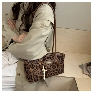 Detail of leopard print suede shoulder bag with wood bead tassel on a model