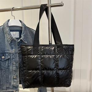 Chic black quilted puffer tote bag with wide straps shown on denim jacket background