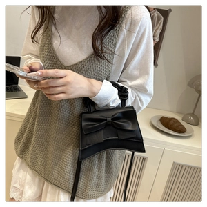 Detail of black bow handbag featuring a unique crescent base and twisted knot handle