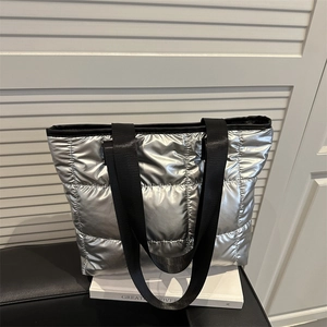 Metallic silver quilted tote bag with black strap on white book, sleek minimalist style