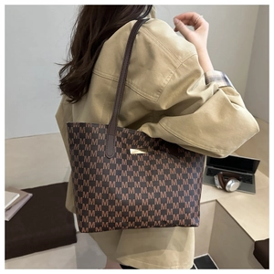 Close-up of brown monogram tote bag with gold hardware shown in a minimalist office setting