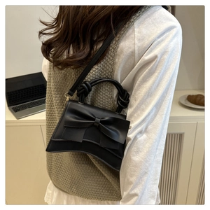 Detail of black trapezoid bag featuring large leather bow and unique knotted top handle
