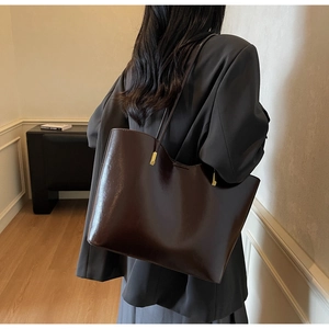 Detail of dark brown glossy leather tote bag with thin straps on professional attire