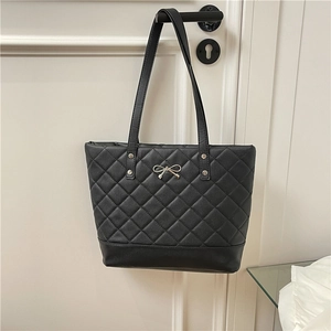 Quilted black tote bag with silver bow accent hanging on a door for daily commute