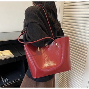 Close-up of bright red glossy tote bag with gold hardware on black knit wear