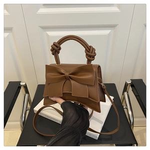 Detail of dark brown leather handbag with a large bow and unique knotted handle on a book