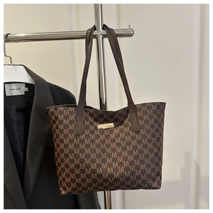 Detail view of brown tote bag with M-pattern monogram and gold metal plate decorative accent