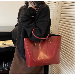 Detail of dark red glossy leather tote bag with gold hardware and slim shoulder strap