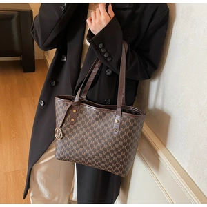Detail of brown monogram tote bag with gold metal M pendant and leather shoulder strap