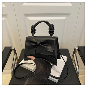 Detail of black crossbody bag with large bow decoration and unique twisted handle design