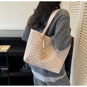 Detail of cream tote bag featuring embossed M pattern and gold circular metal charm
