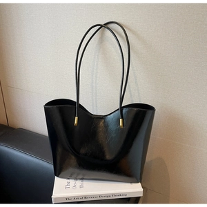 Detail of a black oil-wax leather tote bag with elegant gold hardware on a book