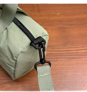 Detail of sage green nylon cylinder bag showing black zipper and metal swivel hook