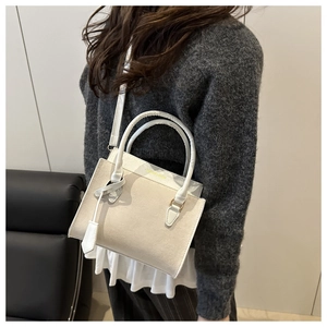 Close-up of cream faux suede handbag with gold lettering held by a model in grey knitwear