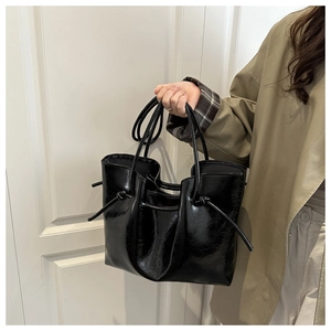 Dettaglio della borsa tote in vernice nera lucida con nodo decorativo e manici sottili