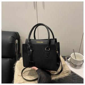 Detail of black faux suede tote with golden lettering and metal hardware on soft fabric